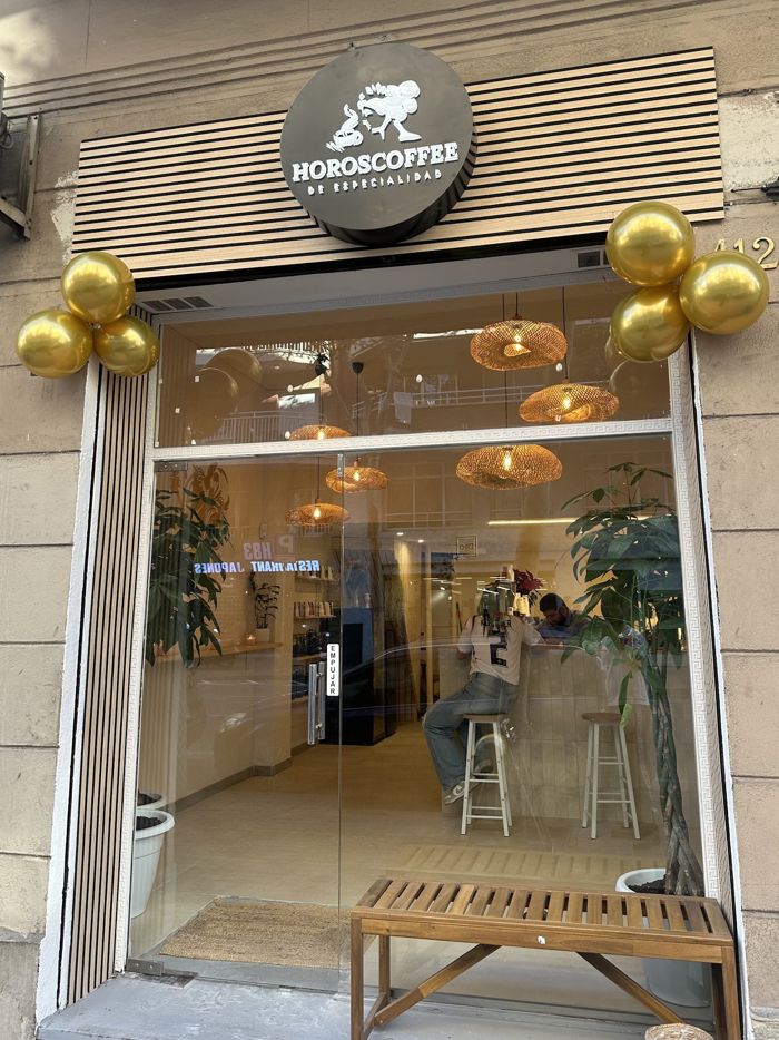 Fachada de HOROSCOFFEE en el Carrer del Rosselló, con el logo redondo sobre la puerta de cristal y lámparas de ratán dentro